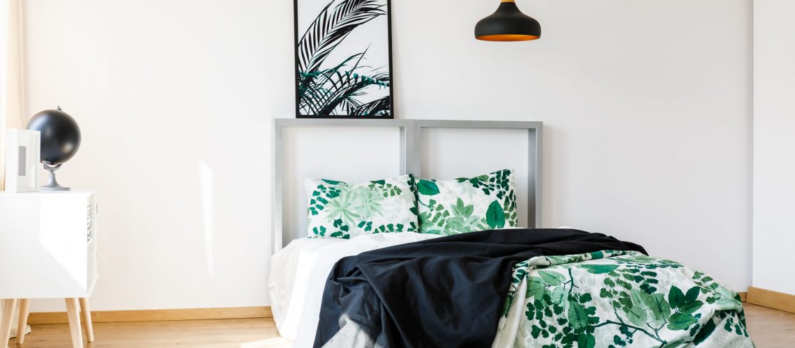 Cozy bed with floral green and white bedding and black blanket